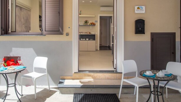 The exterior of Rossy Palace, featuring a covered outdoor seating area with two tables and chairs, a view into the interior, and a sign indicating the location as Amalfi Coast Suite. - Rossy Palace4 - Amalficoast Suites (Agerola)