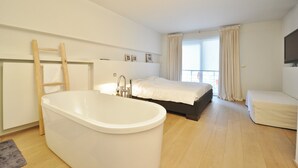 A modern bedroom with a large bathtub, a bed, and a small sofa. - Apartment in Duinbergen by the Seafront (Knokke-Heist)