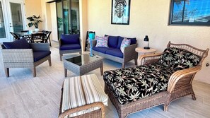 A furnished living area with wicker furniture, a glass coffee table, and a sofa with patterned cushions.