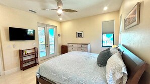 A bedroom with a bed, a dresser, a TV, a ceiling fan, and a window with blinds.