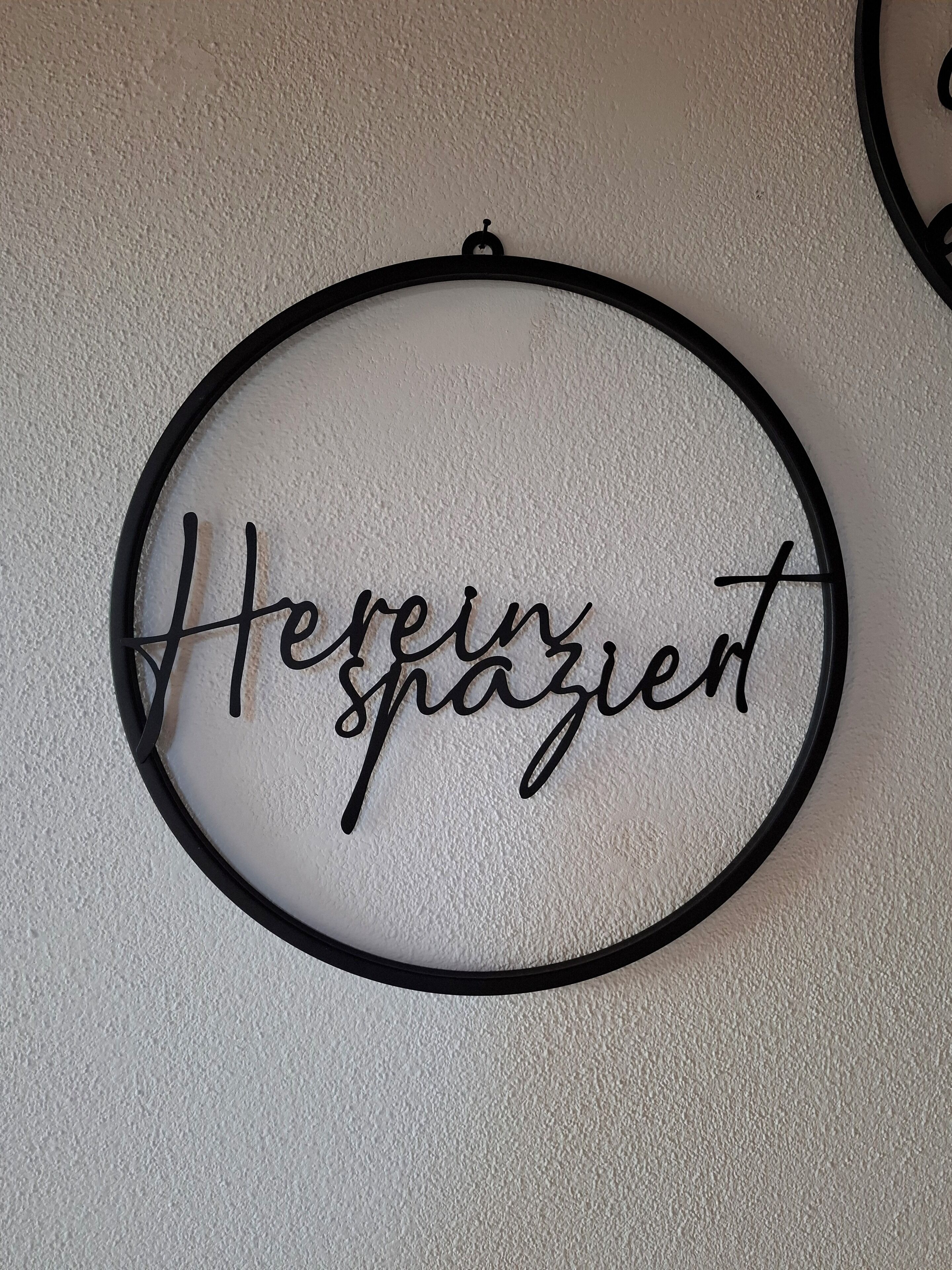 Decoració mural circular amb el text "Hierin spaziert" en lletra cursiva.