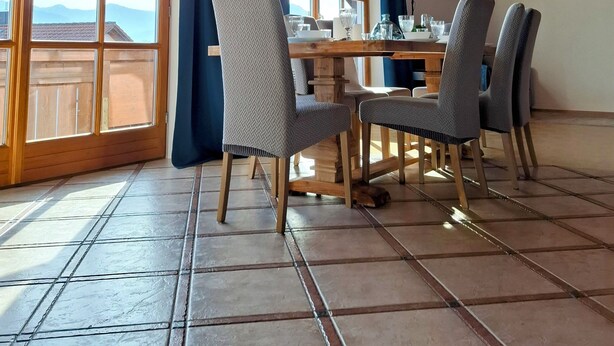 Un espace repas avec une table et des chaises en bois, de grandes fenêtres et un plafond haut avec des poutres apparentes.