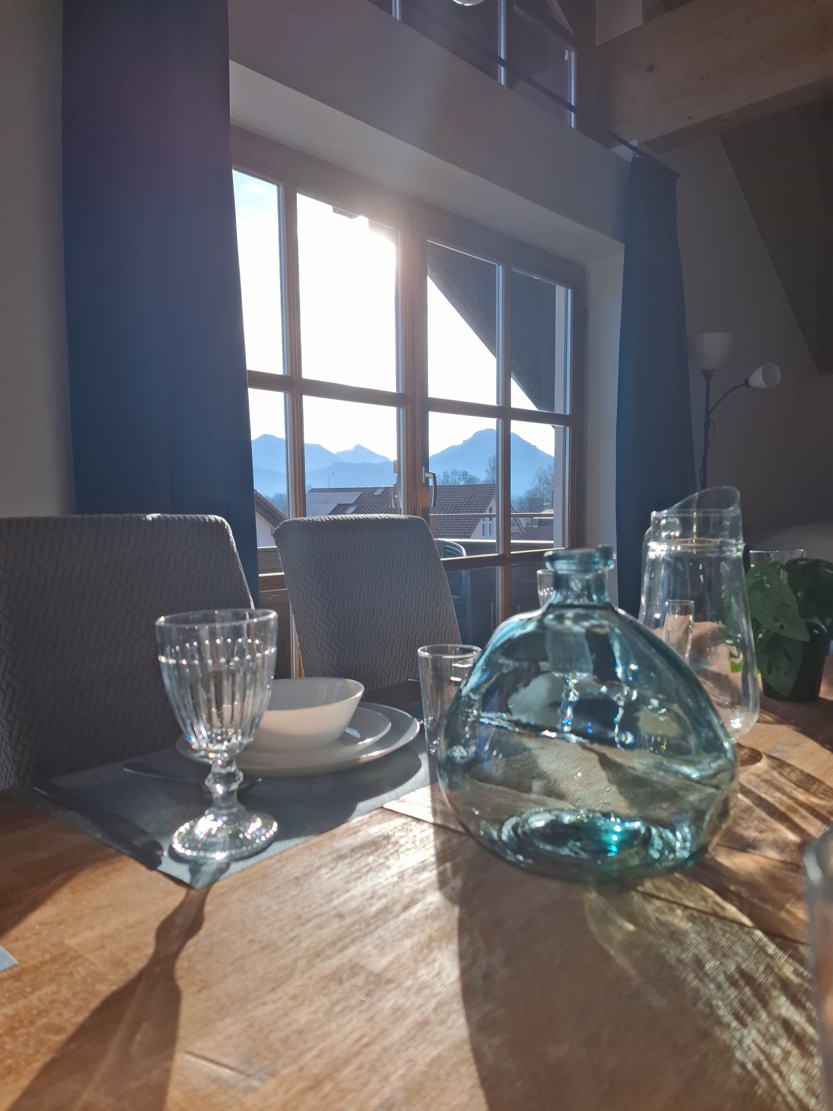 A dining table with a view of mountains through large windows, a glass pitcher, and a bowl.