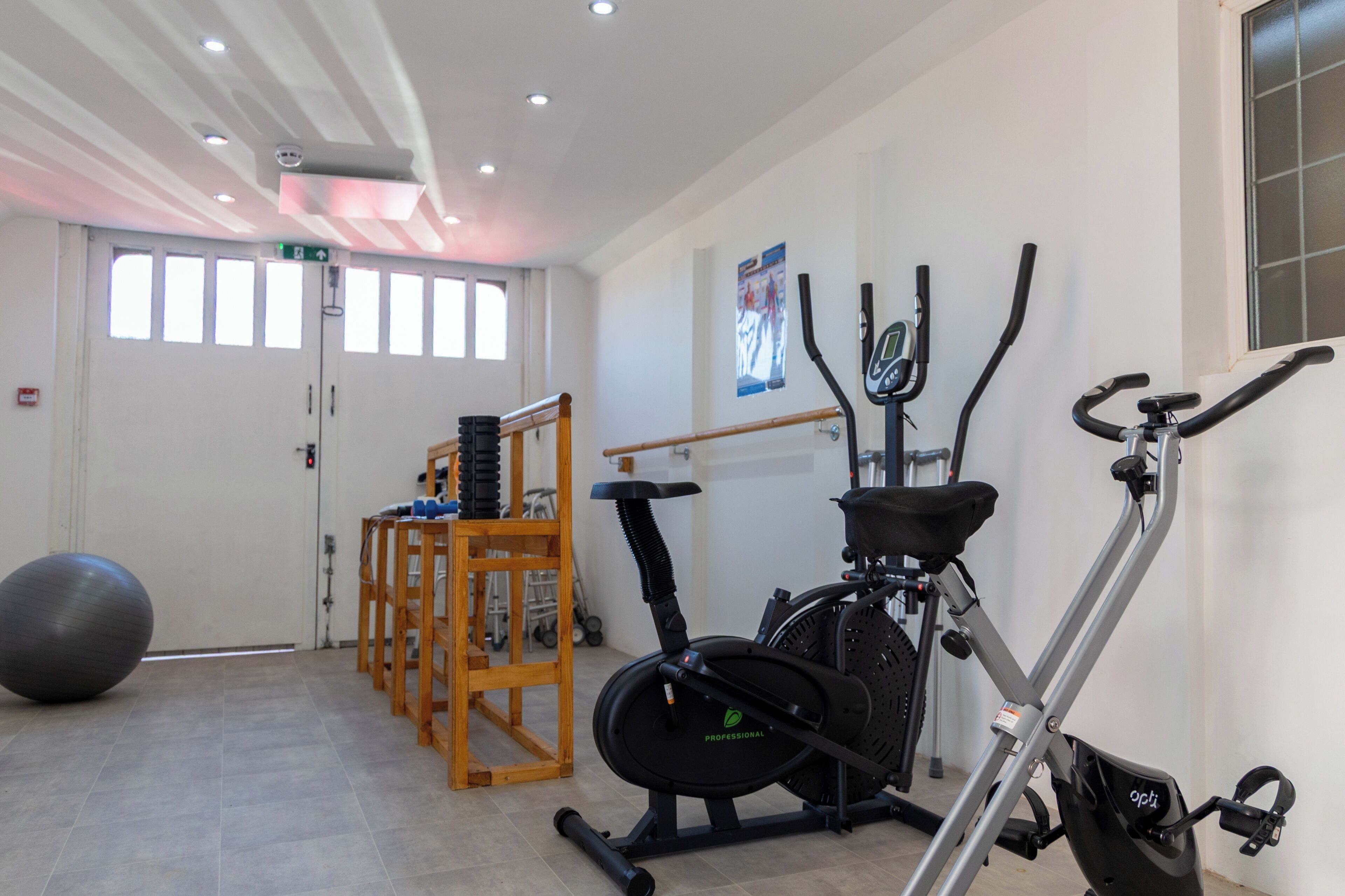 Een fitnessruimte met trainingsapparatuur, een grote fitnessbal en een houten stoel.