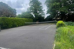 Un court de tennis avec un filet au centre, entouré de verdure et d’arbres.
