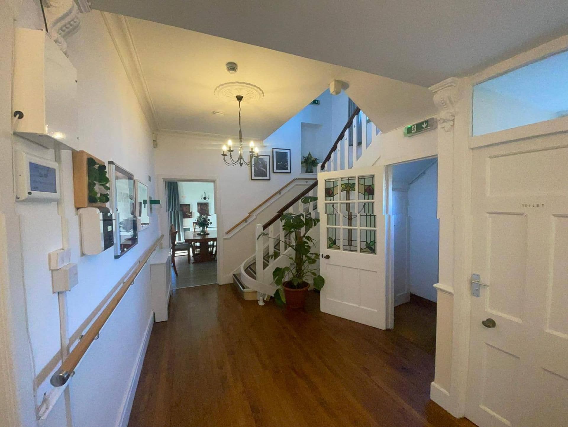 A hallway with a wooden floor, a staircase, and a door marked 'TOILET'.
