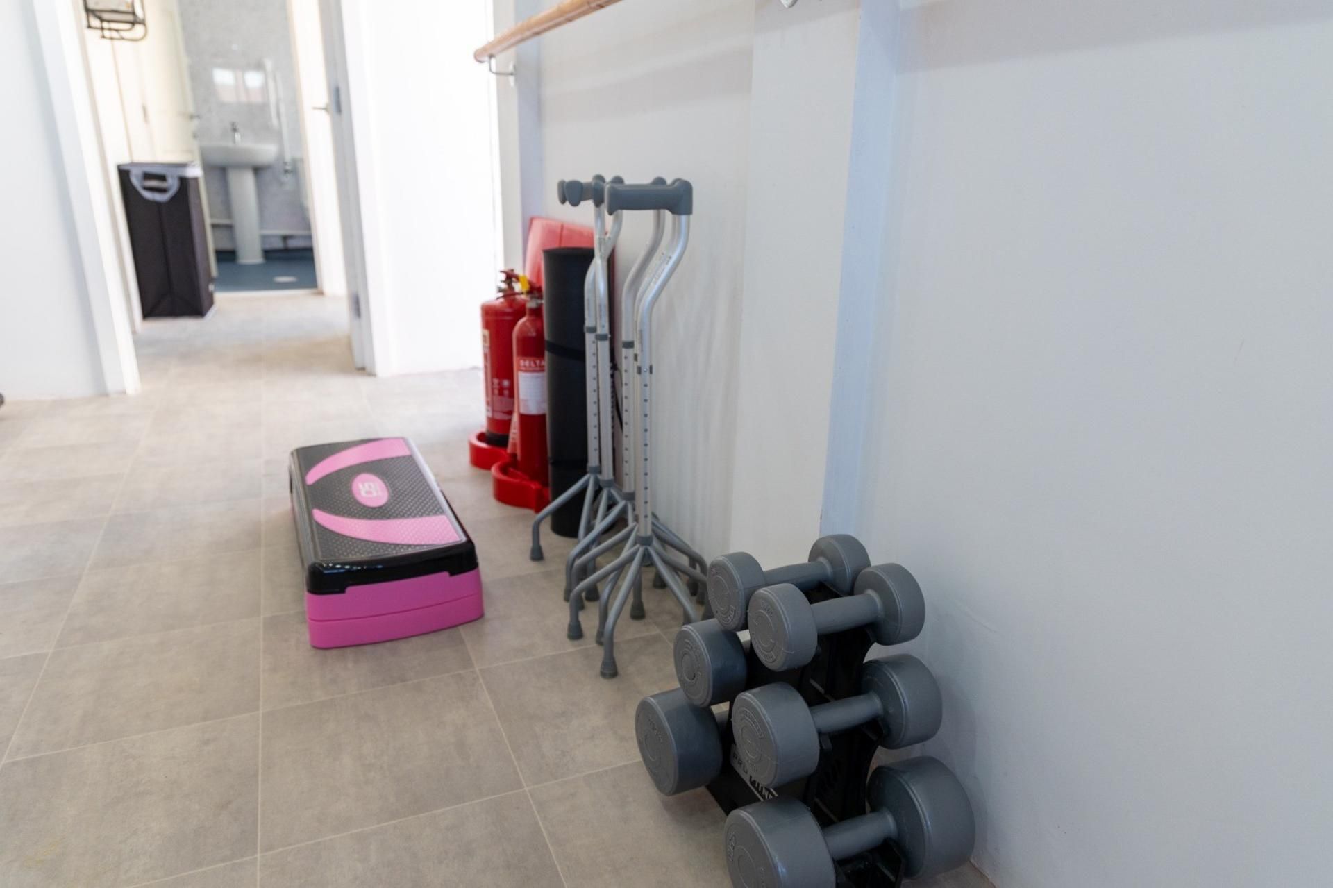 Zona de gimnasio con equipo de ejercicio, incluyendo una plataforma de step rosa, mancuernas y una estructura para sentadillas.