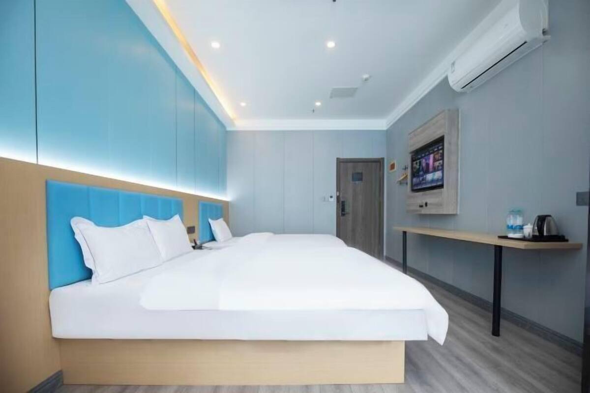 A modern hotel room with a large bed, a TV mounted on the wall, and a small table with a kettle.