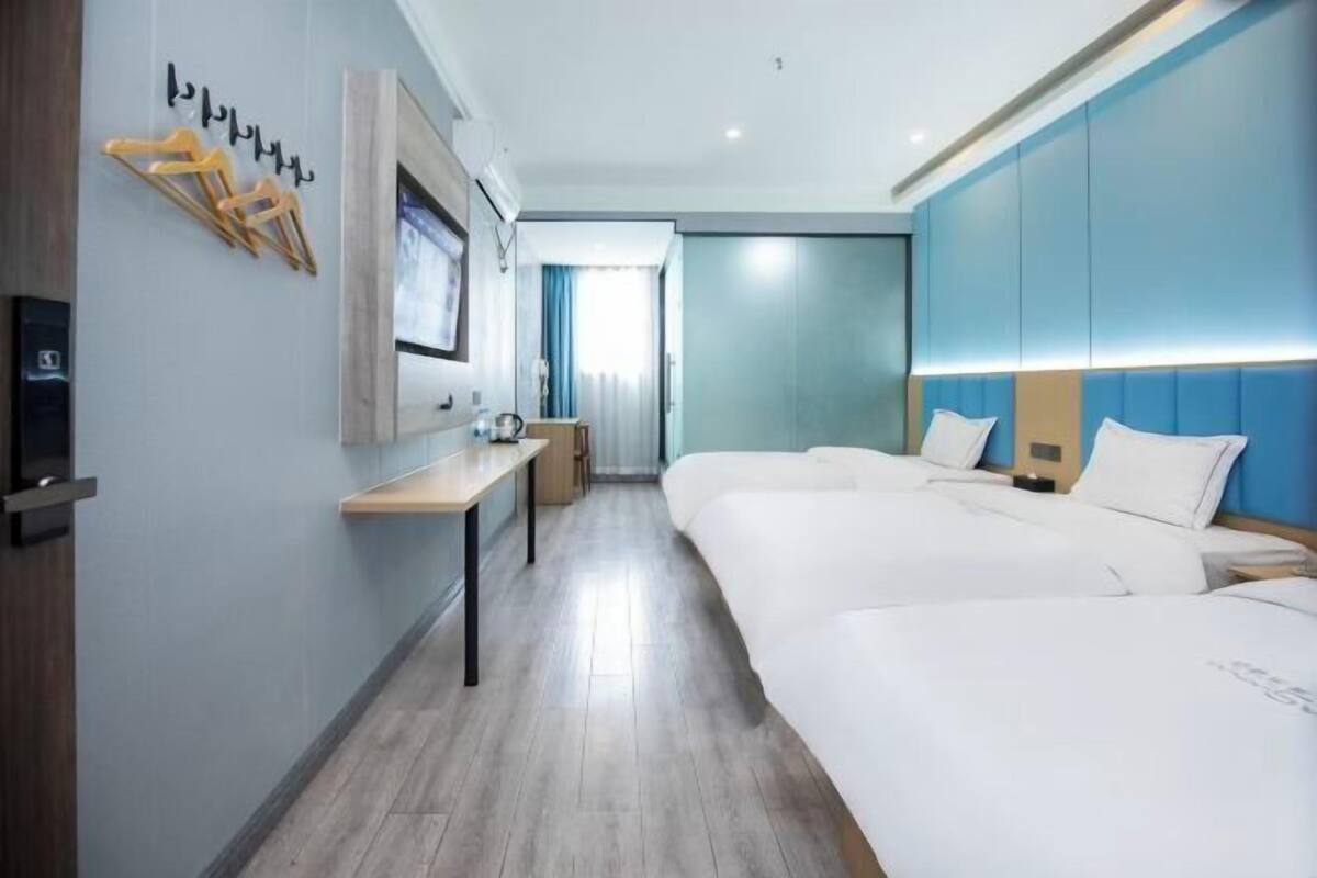 A hotel room with two beds, a desk, a TV, and a window with curtains.