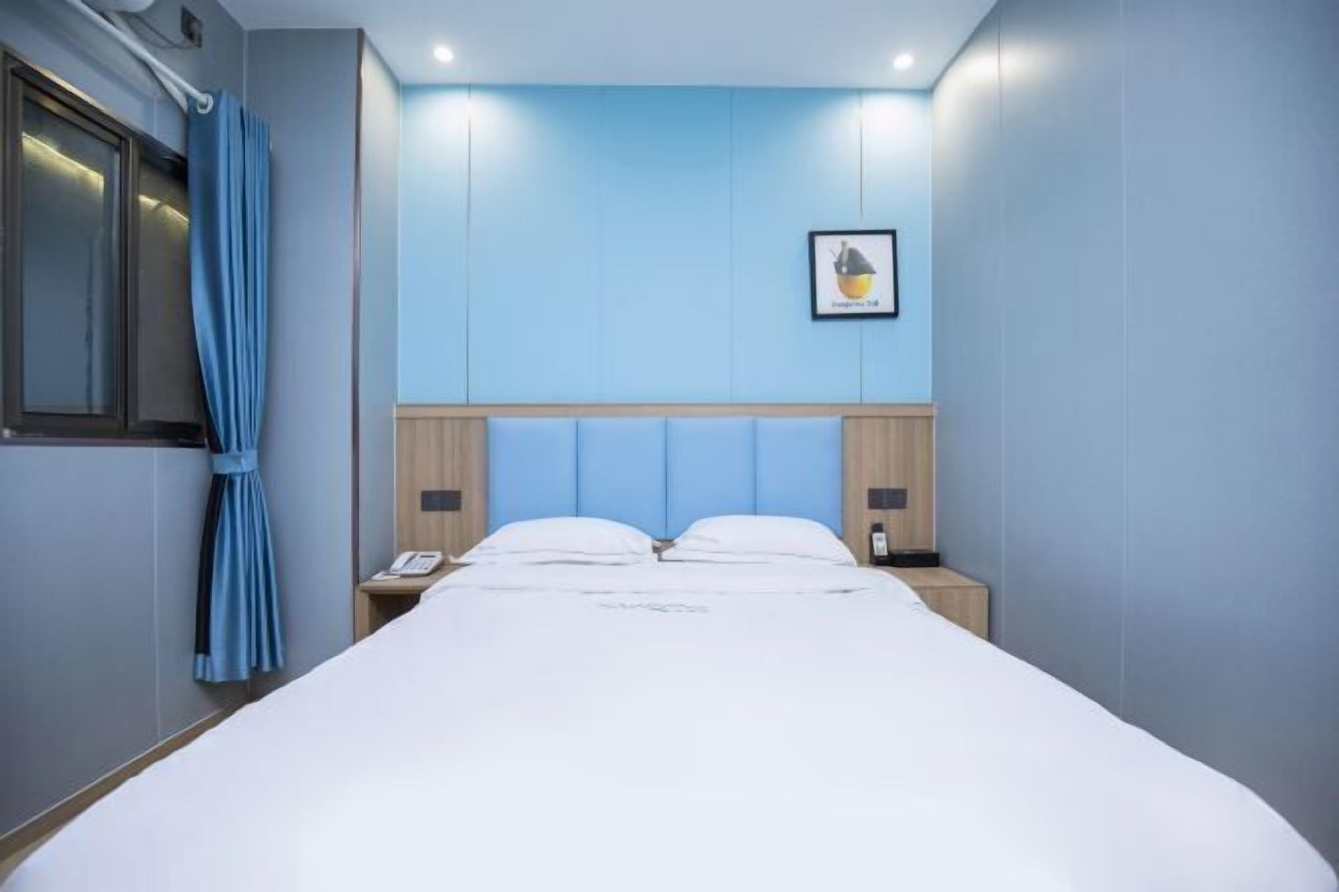 A hotel room with a large bed, a headboard, a bedside table, a phone, and a curtain.