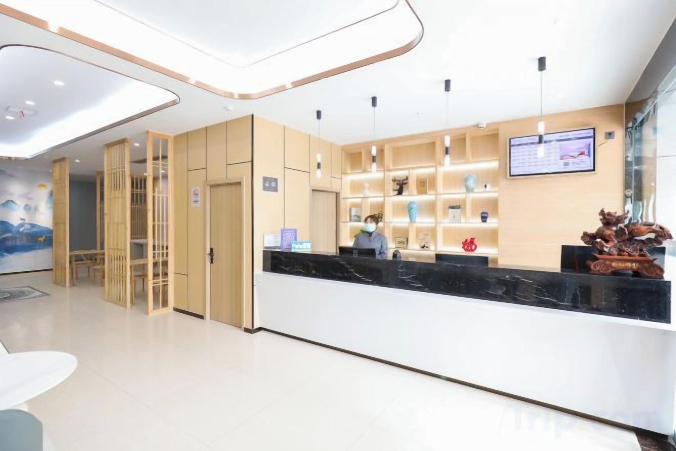 A modern hotel reception area with a reception desk, a seating area, and a wall-mounted television.