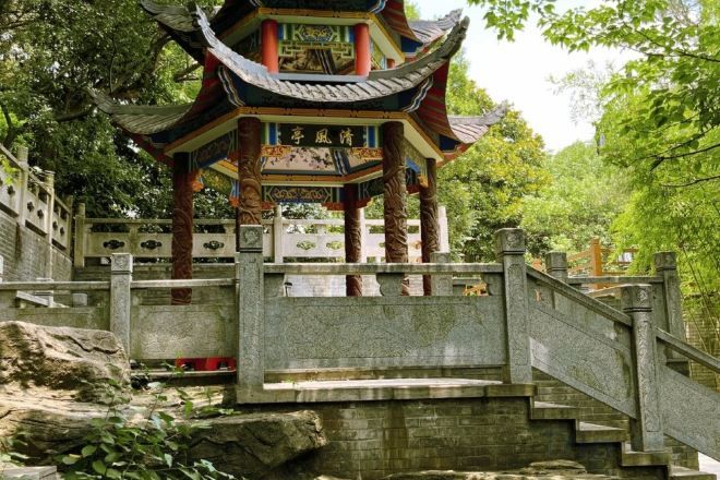 A traditional Chinese pavilion with a tiled roof, surrounded by stone steps and a stone railing.