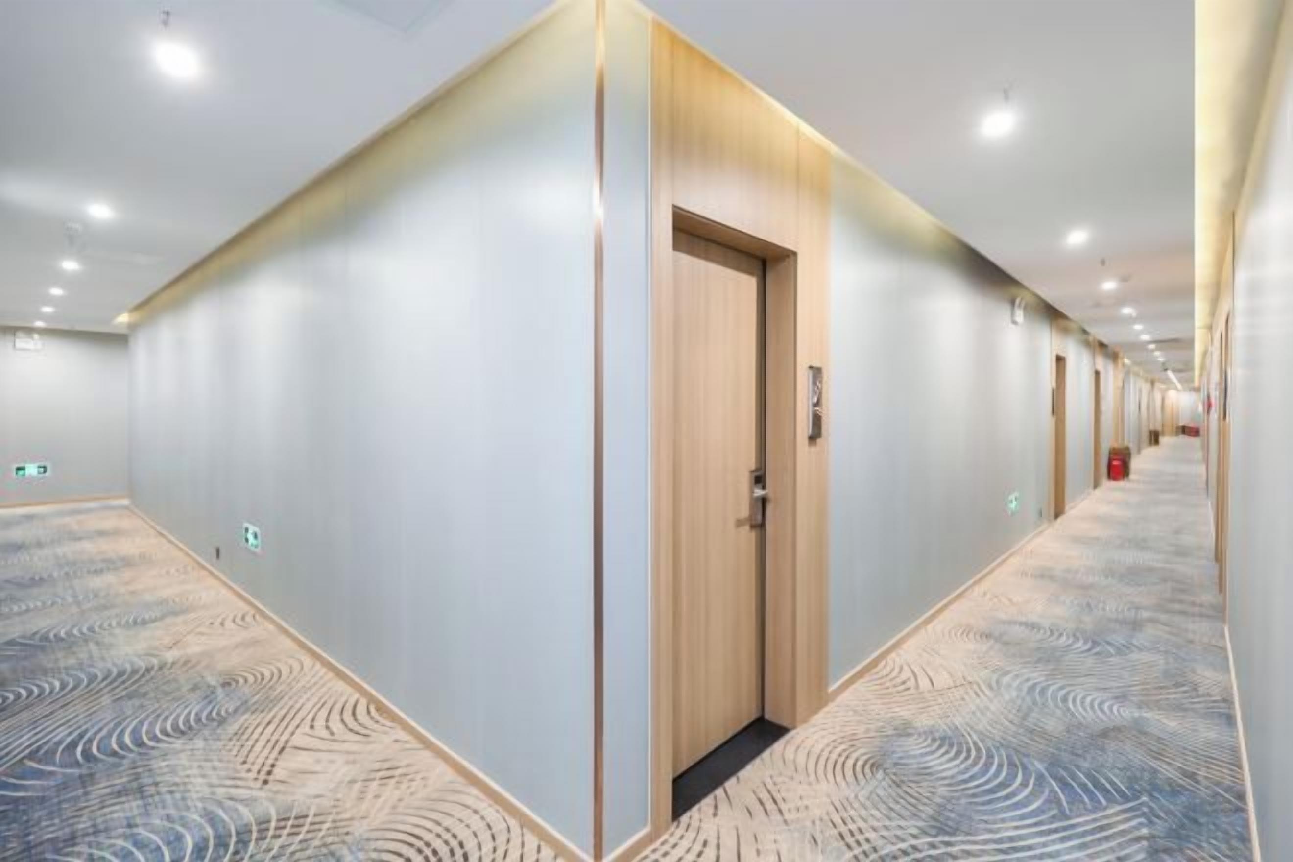 A hotel corridor with a patterned carpet, wooden doors, and recessed lighting.