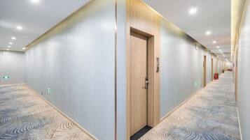 A hotel corridor with a patterned carpet, wooden doors, and recessed lighting.
