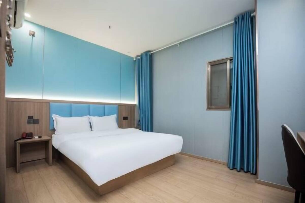 A modern hotel room with a large bed, a nightstand, a desk, and a window with curtains.