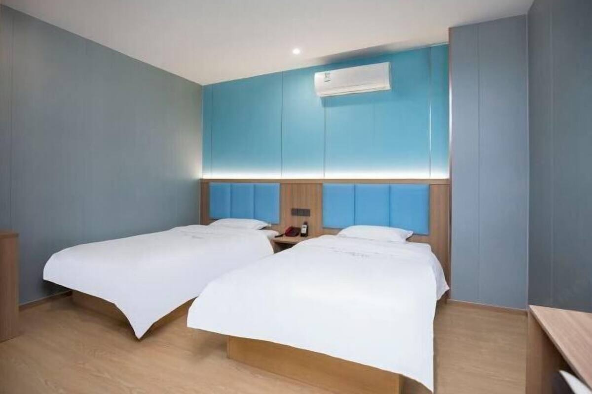 A hotel room with two beds, a wooden headboard, a nightstand, and an air conditioning unit.