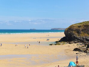 A wide sandy beach with a rocky outcrop on the right, a clear blue sky, and calm sea. - Bay View Barn (Hayle)