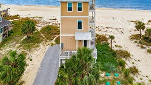 A multi-story beachfront building with a balcony, a beach access sign, and a view of the ocean.