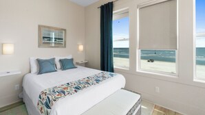 A bedroom with a large bed, a view of the beach, and a window with a curtain.