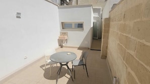 Eine kleine Terrasse im Freien mit einem runden Tisch und zwei Stühlen, einer weißen Wand und einer Steinwand.