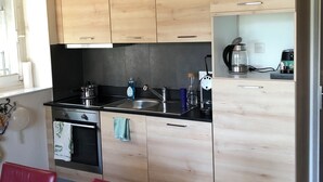 Una cocina moderna con armarios de madera, encimera negra y una zona de comedor con mantel rojo.