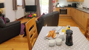 Ett mysigt vardagsrum med en soffa, ett matbord dukat med frukostmat och ett kök i bakgrunden.