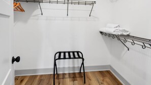 Une petite pièce avec un plancher en bois, un étendoir métallique, une chaise en métal et une porte dotée d’une poignée de porte noire.