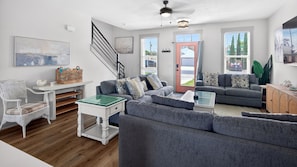 A modern living room with a grey sofa, a glass coffee table, a white side table, a wicker basket, and a staircase. - Private Pool & Game Room • Sleeps 15 • Near 30A, Beach Access & Pier Park (Panama City Beach)