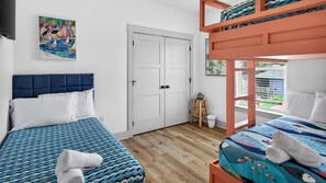 Une chambre d’hôtel avec deux lits, un lit superposé, une porte, un petit tabouret et un tableau au mur.