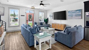 A modern living room with a sectional sofa, a glass coffee table, and a flat-screen TV mounted on the wall.