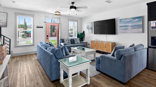A modern living room with a sectional sofa, a glass coffee table, and a flat-screen TV mounted on the wall.