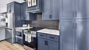 Cocina moderna con armarios grises, un refrigerador de acero inoxidable, un microondas, un horno y una estufa a gas.