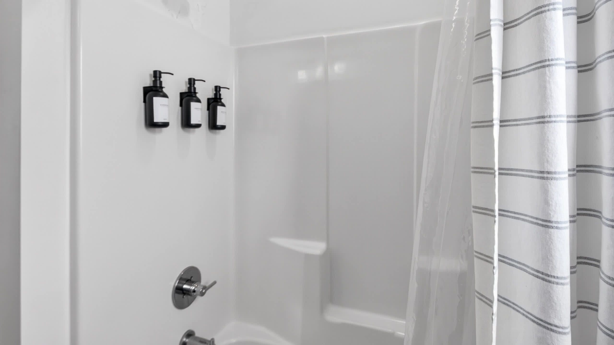 A bathroom with a shower, a toilet, and two black soap dispensers mounted on the wall.