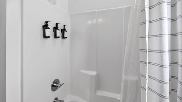 A bathroom with a shower, a toilet, and two black soap dispensers mounted on the wall.