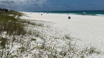 Una playa de arena blanca, vegetación escasa y cielo azul despejado.