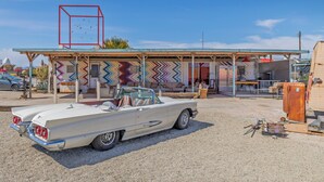 Une voiture décapotable blanche, d’époque, est garée devant un bâtiment aux couleurs vives, dont les murs sont ornés d’un motif en zigzag original.