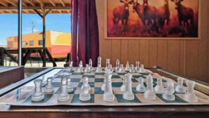 Un jeu d’échecs est installé sur une table en bois, avec un rideau rouge en arrière-plan.
