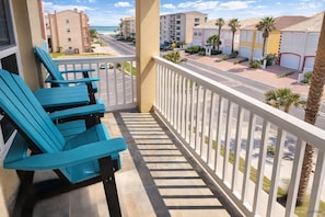 A balcony with blue chairs, a view of a beach, and a street with buildings. - NEW! Cora Lee Beachview 2-Bedroom Condo (South Padre Island)