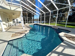 En swimmingpool med klart, blåt vand, omgivet af en overdækket terrasse med stole og et bord.