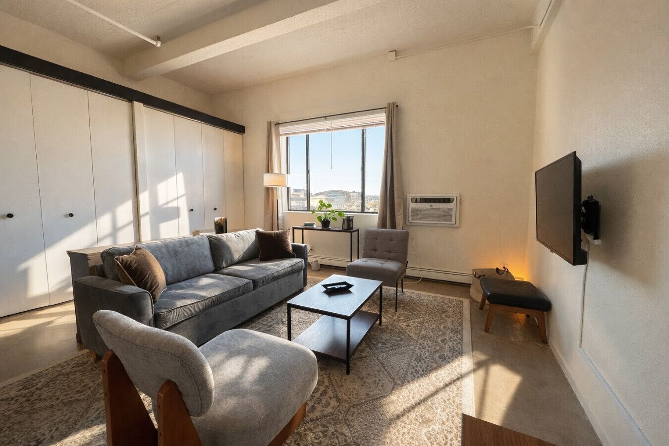 A modern living room with a sofa, armchair, coffee table, and a TV mounted on the wall.
