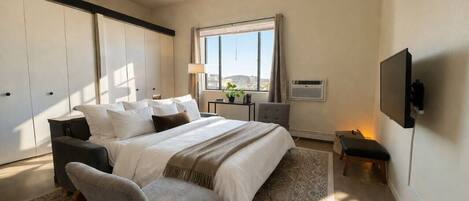 Un dormitorio con cama, sillas a los lados, un escritorio, un televisor y una ventana con vistas.