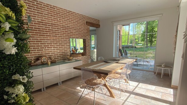 Una cocina moderna con pared de ladrillo, un comedor con una mesa grande y sillas, y vistas al exterior.