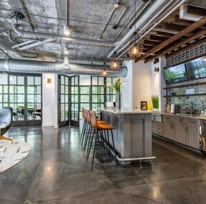 A modern kitchen with stainless steel appliances, a bar area with stools, and large windows offering views of greenery.