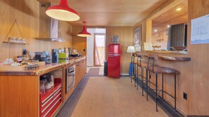 Cucina con mobili in legno, frigorifero rosso, angolo bar con sgabelli e lampadario.