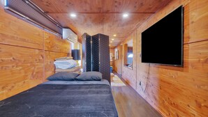 Interno di una baita di legno con un letto, una televisione montata a parete e un soffitto in legno.