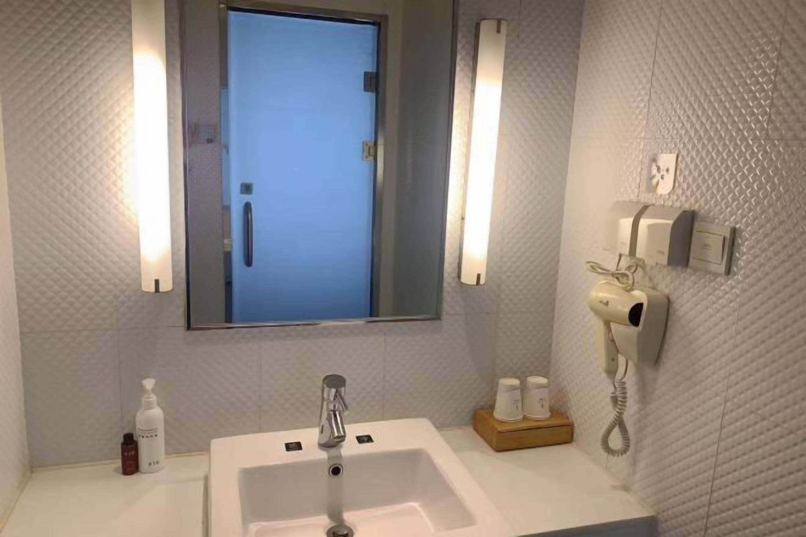 Un baño con un espejo grande, un lavamanos, un secador de pelo y un teléfono en la pared.