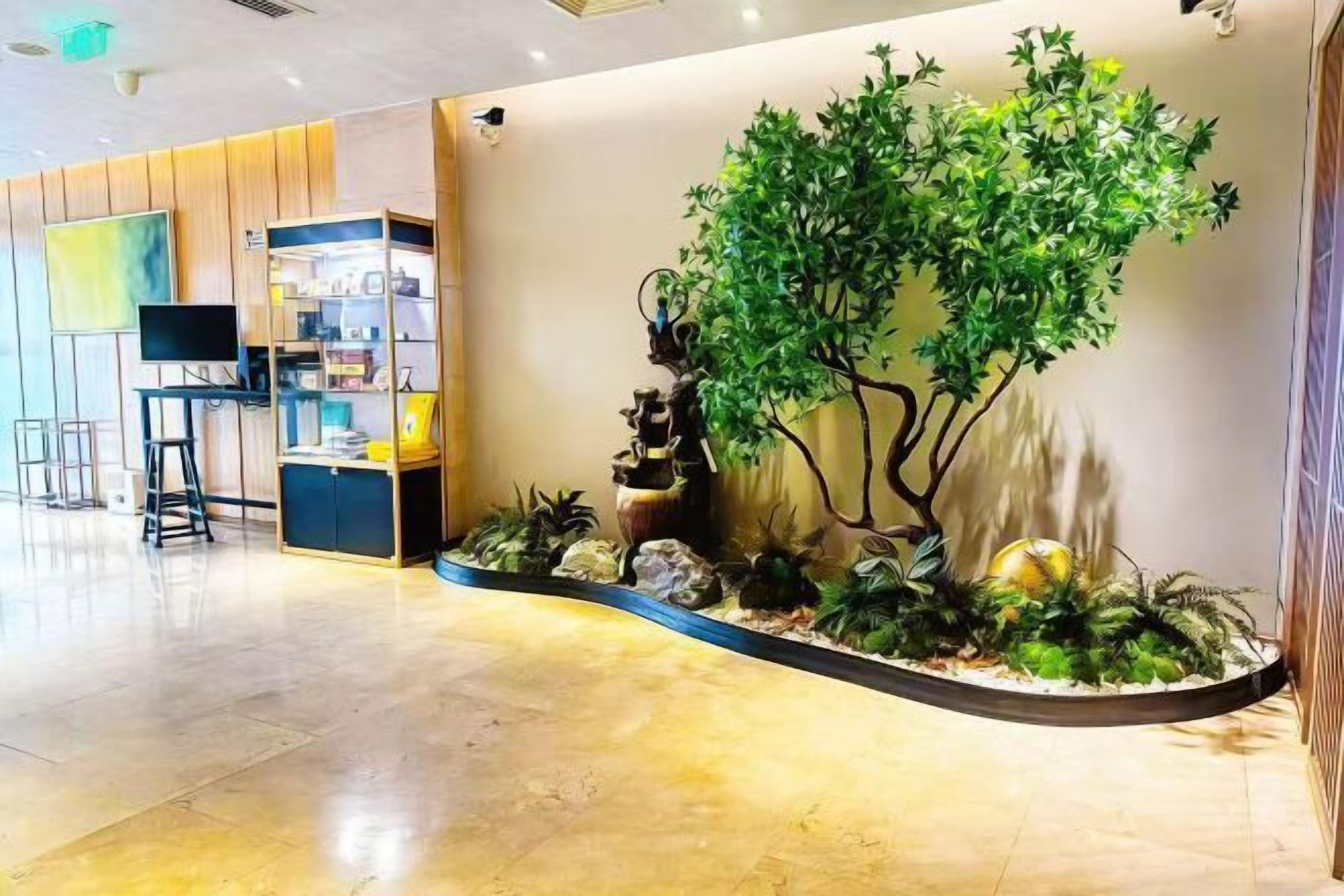 A reception area with a curved wall, a large artificial tree, and a small waterfall feature.