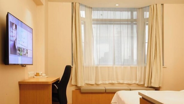 A hotel room with a desk, a chair, a bed, a window with curtains, and a television on the wall. - Meihao EZZI Hotel (Tianjin Youyi Road Wudadao) (Tianjin)