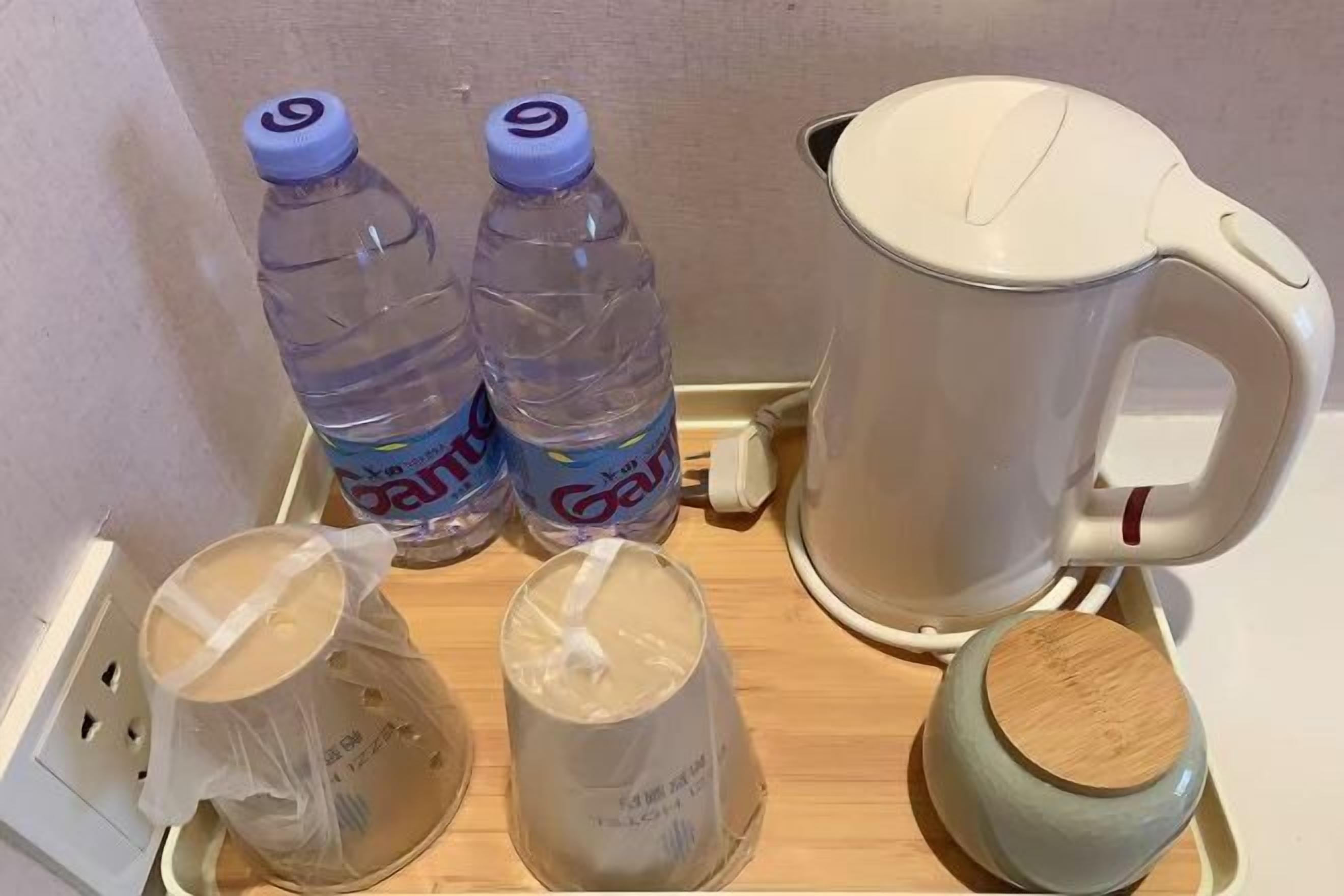 A kitchen area with a kettle, two water bottles, and two containers on a tray.