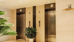 A modern elevator area with three elevators, each marked with a number. A potted plant is placed in the center. - Meihao EZZI Hotel (Tianjin Youyi Road Wudadao) (Tianjin)